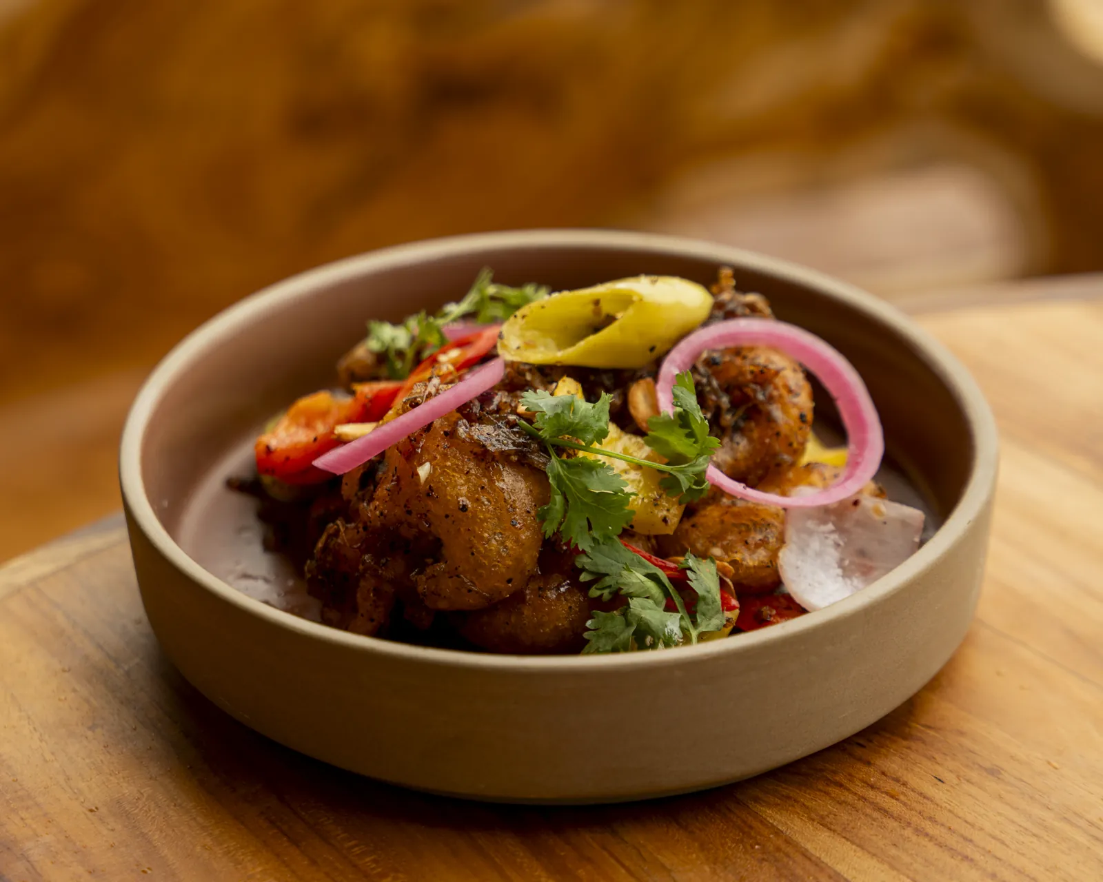 A clay bowl of spiced prawns with tomato, pickled onion and coriander at Nava