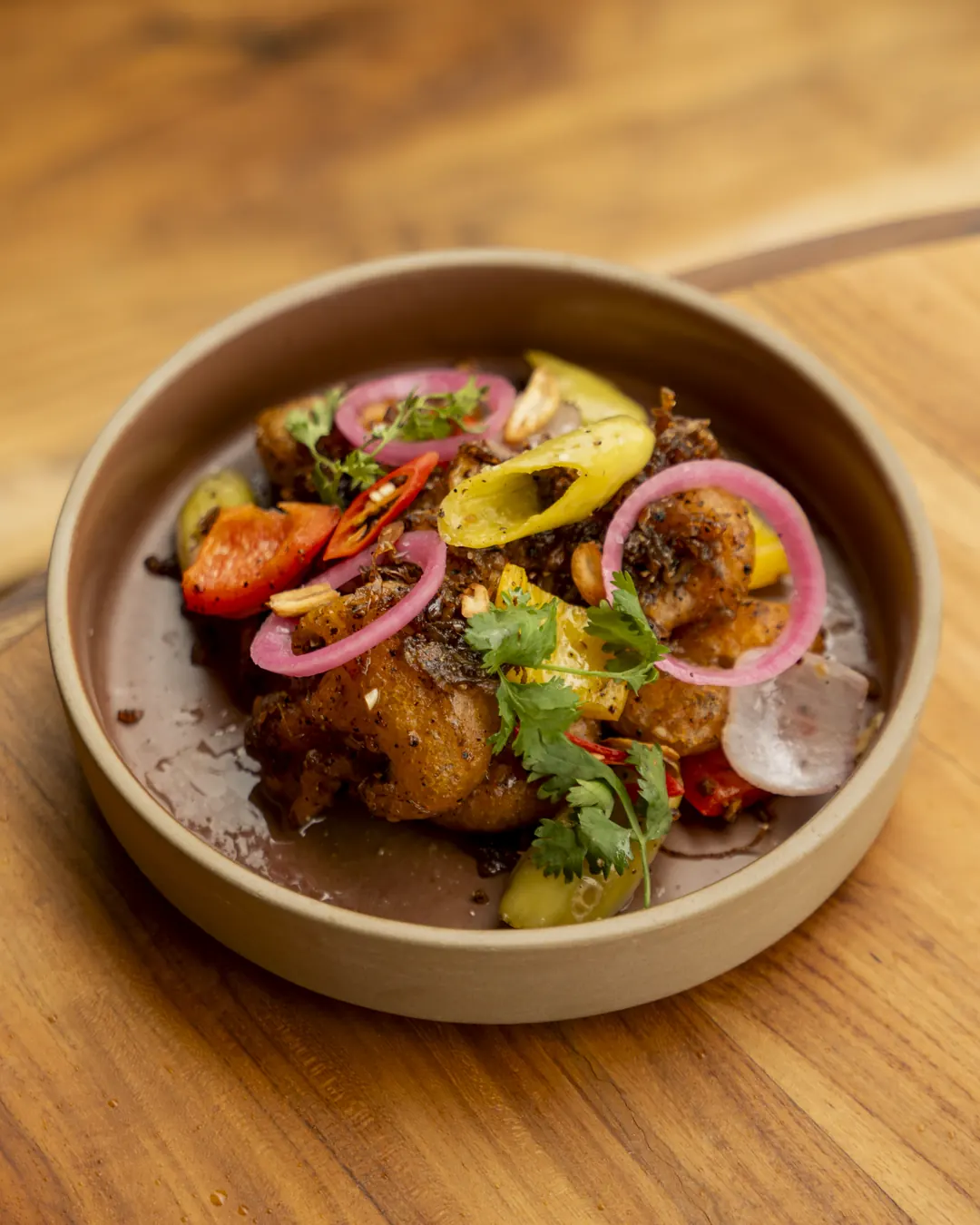 A clay bowl of spiced prawns with tomato, pickled onion and coriander at Nava