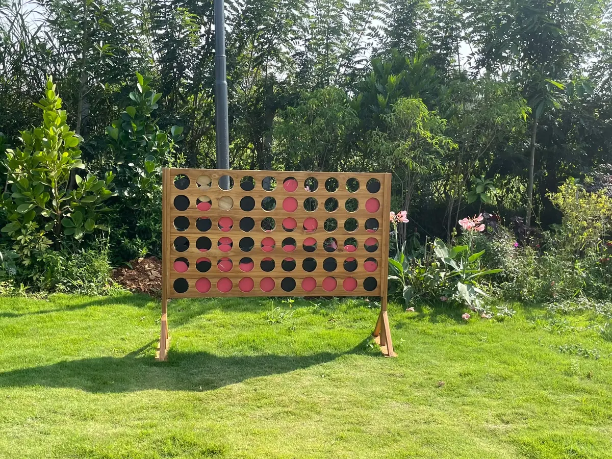A giant wooden Connect 4 board standing on the lawn among the plants