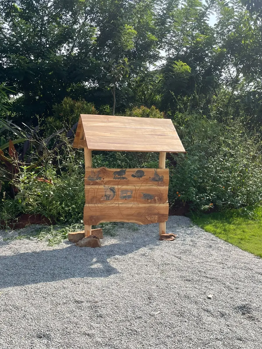 A small timber hut-shaped board with natural objects set into it, in the garden
